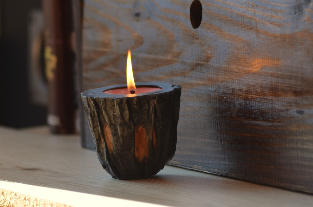 Vela artesanal encendida en un portavelas de cera texturizada sobre madera